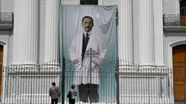 La gente mira una imagen del médico venezolano José Gregorio Hernández afuera de la iglesia La Candelaria, que alberga sus restos, en Caracas (Venezuela), el 21 de junio de 2020. (Federico Parra/AFP vía Getty Images)