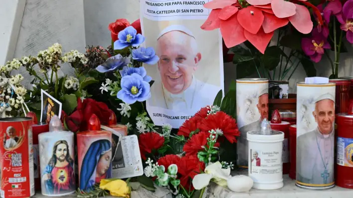 Velas, flores y un retrato del papa Francisco se colocan en la estatua de Juan Pablo II afuera del hospital Gemelli, donde el Papa Francisco está hospitalizado en Roma, el 22 de febrero de 2025. (Alberto Pizzoli/AFP vía Getty Images)