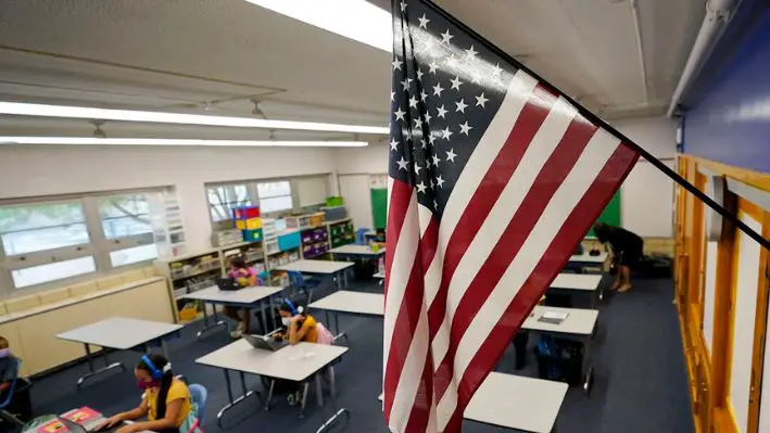 Una bandera estadounidense cuelga en un aula mientras los estudiantes trabajan en computadoras portátiles en la Escuela Primaria Newlon, en Denver, el 25 de agosto de 2020. (David Zalubowski/AP Photo)