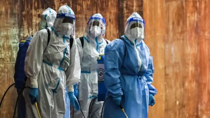 Trabajadores que manipulan desinfectante observan junto a una zona residencial bajo confinamiento por Covid-19 en el distrito de Huangpu, Shanghái, el 4 de junio de 2022. (Hector Retamal/AFP vía Getty Images)