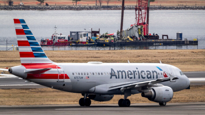 Un avión se prepara para despegar en la pista mientras un barco de salvamento con restos de un accidente se retira del lugar en el río Potomac de una colisión en el aire entre un avión de American Airlines y un helicóptero Black Hawk, en el Aeropuerto Nacional Ronald Reagan de Washington, el 5 de febrero de 2025, en Arlington, Virginia. (Ben Curtis/AP Photo).