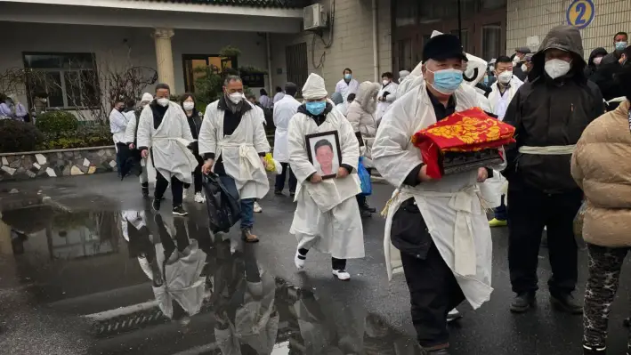 Un doliente lleva los restos incinerados de un ser querido mientras él y otros visten la ropa blanca tradicional durante un funeral en Shanghái, China, el 14 de enero de 2023. (Kevin Frayer/Getty Images)