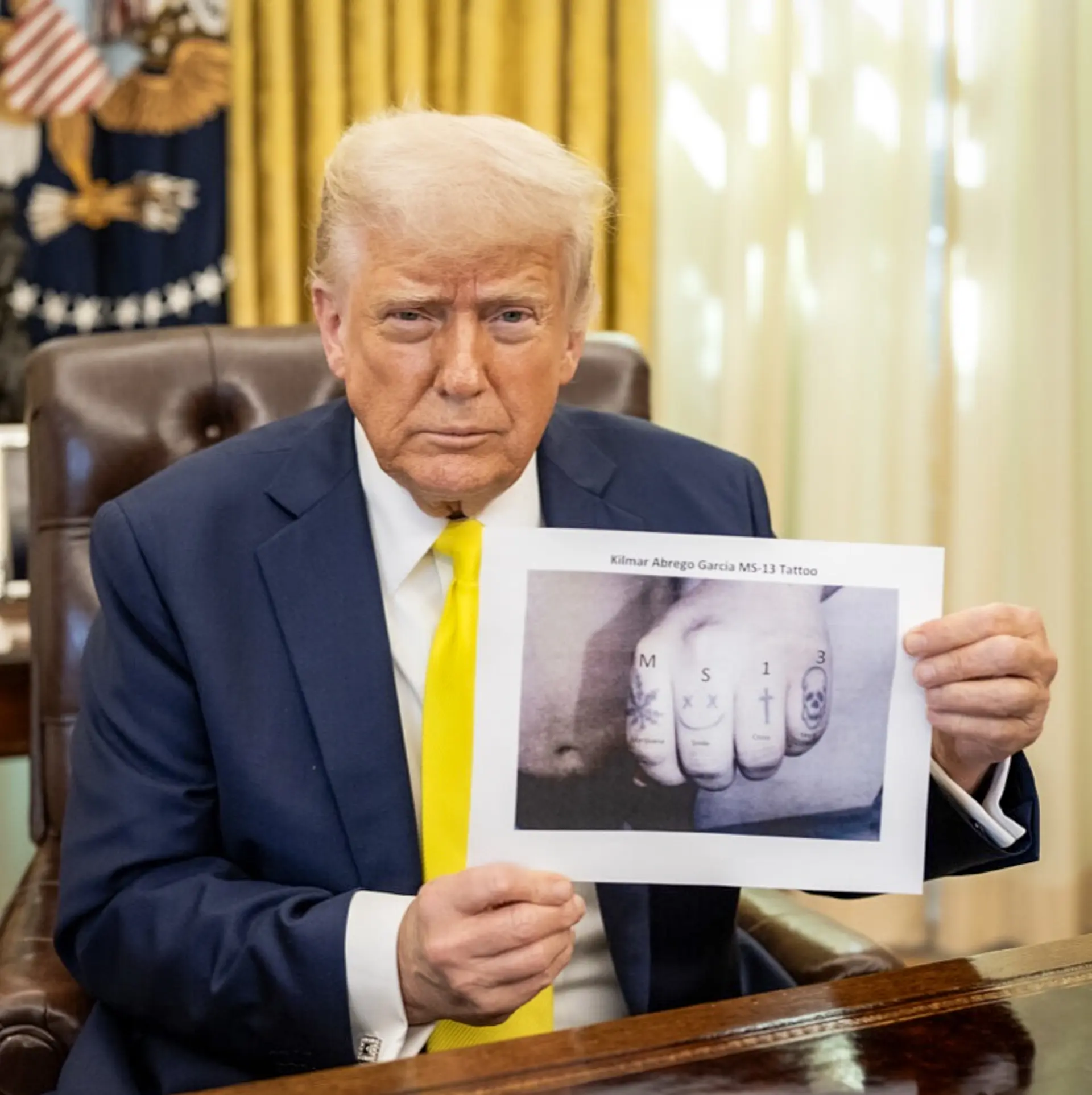 El presidente Donald Trump sostiene una fotografía de los tatuajes en los nudillos de Abrego García, con las letras "M", "S", "1" y "3" añadidas digitalmente a la imagen. (Dominio público).