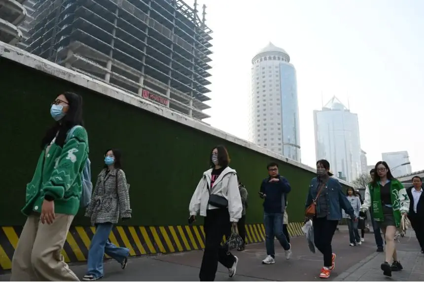 Varias personas pasan por delante de edificios en el distrito central de negocios de Beijing mientras se dirigen al trabajo el 11 de abril de 2025. (Greg Baker/AFP vía Getty Images)