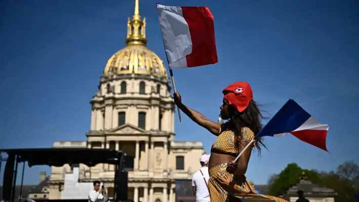 Un asistente con un gorro frigio rojo sostiene banderas nacionales francesas frente a la cúpula dorada de Los Inválidos, antes de una manifestación en apoyo de la presidenta del grupo parlamentario Rassemblement National, Marine Le Pen, en París, el 6 de abril de 2025. (Julien de Rosa/AFP)