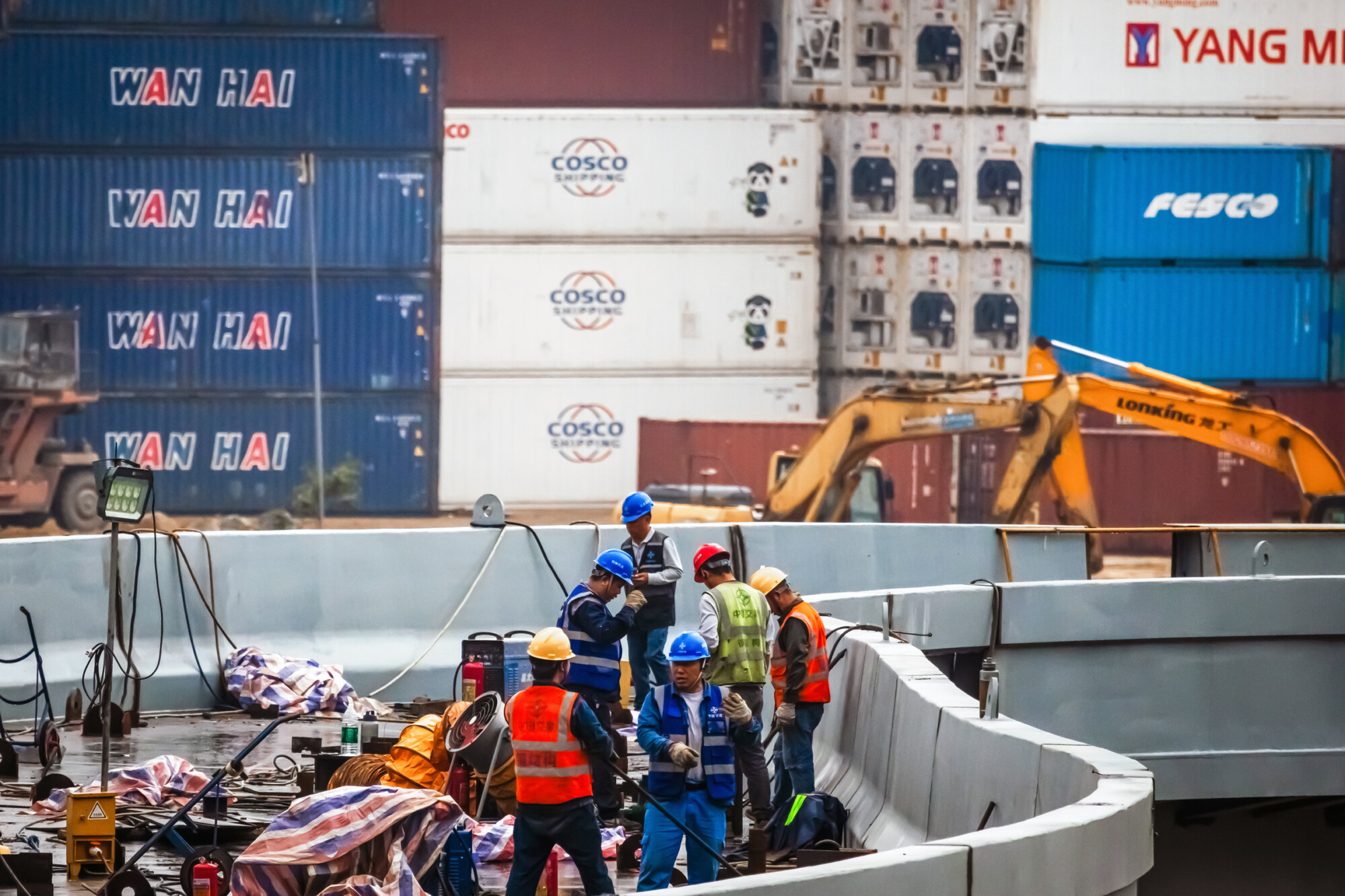 Obreros trabajan en una obra frente a contenedores de transporte en la Terminal Internacional de Contenedores de Yantian, en Shenzhen, provincia de Guangdong, China, el 12 de abril de 2025. China ha impuesto nuevos aranceles de represalia a los productos estadounidenses, aumentando los aranceles al 125 por en respuesta a los últimos aranceles estadounidenses del 145 por ciento. La escalada de tensiones comerciales ha tensado aún más el sector exportador chino y ha agravado la crisis de desempleo. (Cheng Xin/Getty Images, Jade Gao/AFP a través de Getty Images).