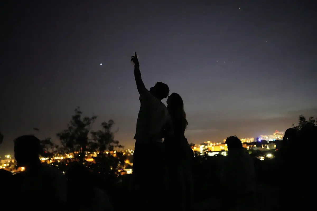 Una joven pareja se encuentra de pie sobre un muro mirando al cielo en un mirador con vistas a Lisboa durante un apagón nacional, el 28 de abril de 2025. (Armando Franca/AP Photo).