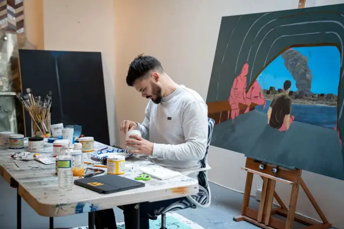 Andrei Kozlov mezcla pintura junto a un cuadro que representa su cautiverio, en un estudio de Nueva York, el 24 de abril de 2025. (Samira Bouaou/The Epoch Times)