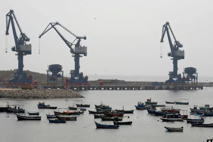 Barcos pesqueros tradicionales anclados en el puerto de la ciudad con las grúas del "megapuerto" de Chancay al fondo, al norte de la capital peruana, Lima, el 29 de octubre de 2024. (Cris Bouroncle/AFP a través de Getty Images).