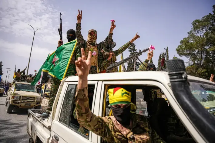 Combatientes de las Fuerzas Democráticas Sirias, lideradas por los kurdos, ondean banderas y hacen gestos de victoria desde un vehículo durante una procesión de convoyes al salir de Alepo, Siria, el 9 de abril de 2025. (MOHAMAD DABOUL/Middle East Images/AFP vía Getty Images)