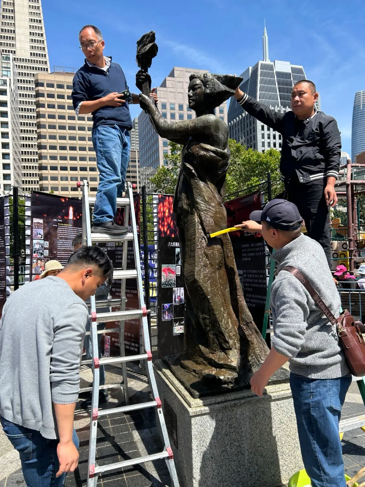 Activistas pro democráticos chinos limpian la estatua de bronce de la Diosa de la Democracia en la plaza de Portsmouth, en San Francisco, el 25 de mayo de 2025. (Nathan Su/The Epoch Times)