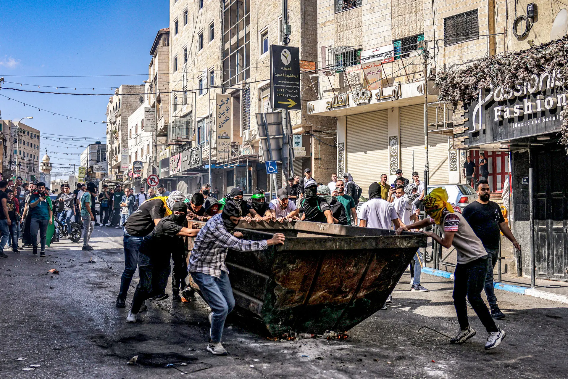 <em>Manifestantes palestinos empujan un contenedor de basura para protegerse durante enfrentamientos con las fuerzas israelíes tras una manifestación en apoyo a Gaza en Hebrón, Cisjordania, el 13 de octubre de 2023. La Corte Suprema está considerando dos casos sobre si las familias de las víctimas de atentados terroristas pueden demandar a la Organización para la Liberación de Palestina (OLP). Hazem Bader/AFP vía Getty Images</em>