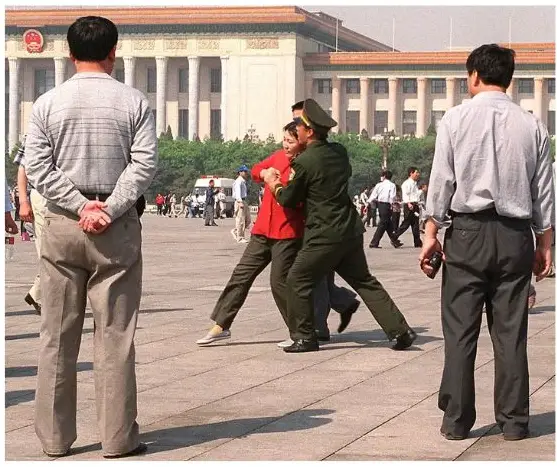 Policías vestidos de civil observan cómo una practicante de Falun Gong se resiste a ser detenida mientras la policía la empuja hacia una furgoneta policial, en la plaza de Tiananmen, Beijing, el 11 de mayo de 2000. (Stephen Shaver/AFP a través de Getty Images)