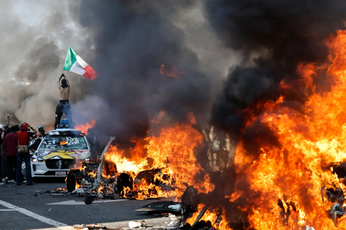 Un manifestante sostiene una bandera mexicana mientras los coches en llamas se alinean en la calle en Los Ángeles, California, el 8 de junio de 2025. (Mario Tama/Getty Images)