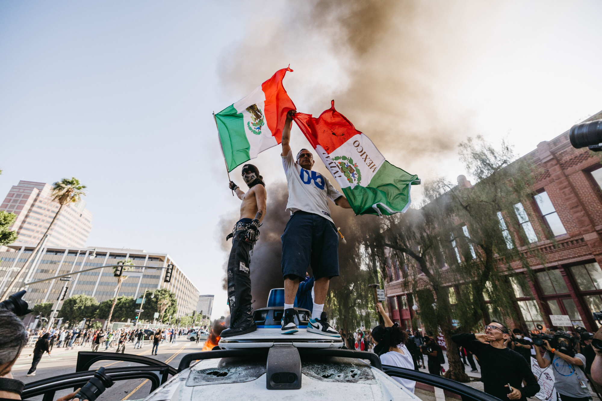Dos manifestantes ondean banderas mexicanas mientras se suben a un vehículo vandalizado de Waymo durante una manifestación en Los Ángeles el 8 de junio de 2025. (David Pashaee/Middle East Images/AFP vía Getty Images)