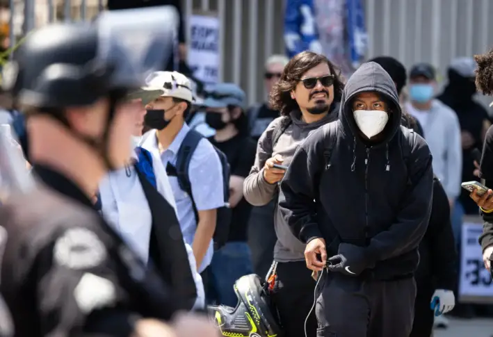 Un hombre se pone guantes frente a una fila de agentes de policía en el centro de Los Ángeles, el 9 de junio de 2025. (John Fredricks/The Epoch Times)