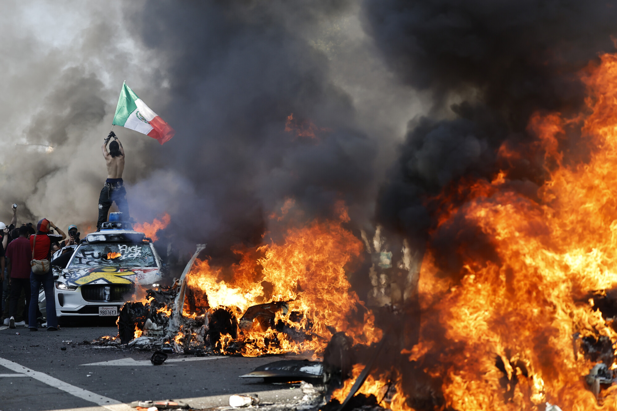 Un manifestante sostiene una bandera mexicana mientras carros en llamas se alinean en la calle el 8 de junio de 2025 en Los Ángeles, California. (Foto de Mario Tama/Getty Images)