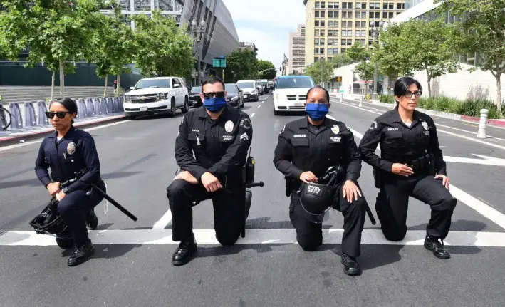 Agentes del Departamento de Policía de Los Ángeles se arrodillan durante una manifestación liderada por ministros baptistas ante el Ayuntamiento en memoria de George Floyd, el 2 de junio de 2020. La ciudad ha pagado hasta ahora 20 millones de dólares para resolver las demandas derivadas de los disturbios de 2020. (Frederic J. Brown/AFP a través de Getty Images)
