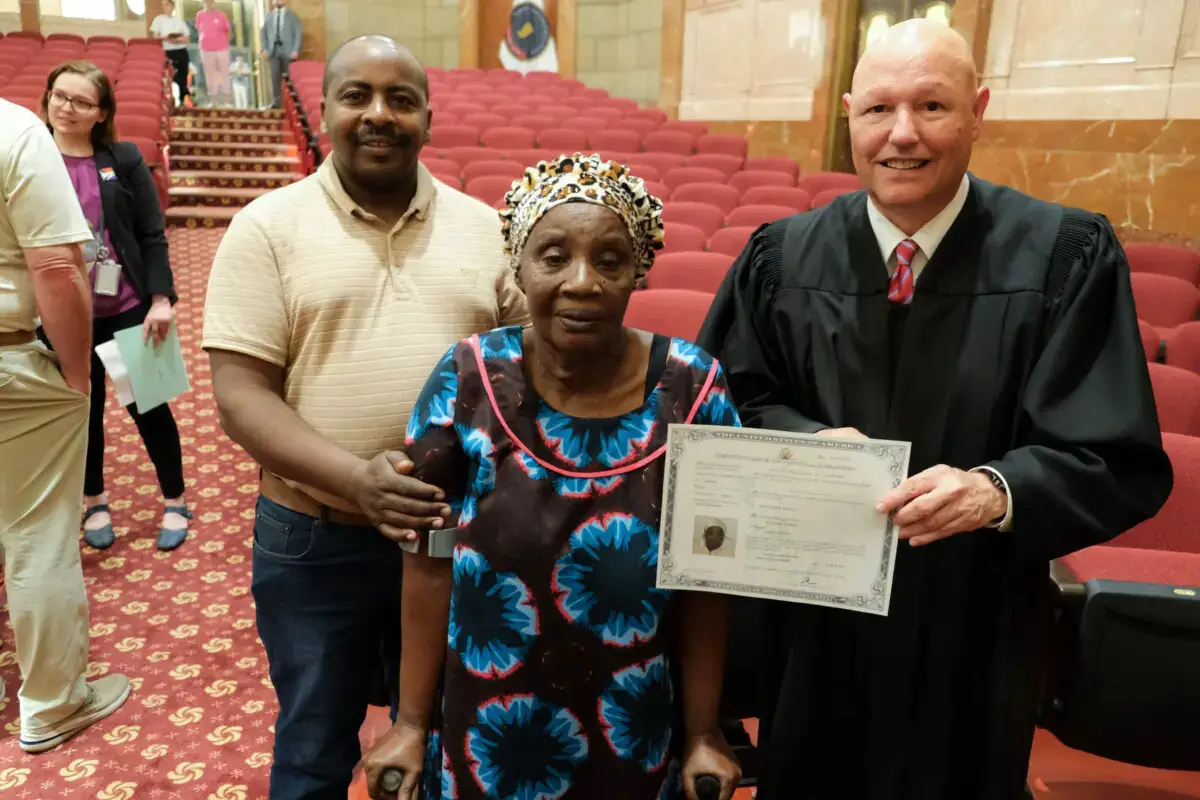 El juez de la Corte de Distrito de Estados Unidos James R. Sweeney II (derecha) entrega un certificado de naturalización a una nueva ciudadana en el Indiana War Memorial de Indianápolis el 26 de junio de 2025. (Lawrence Wilson/The Epoch Times)