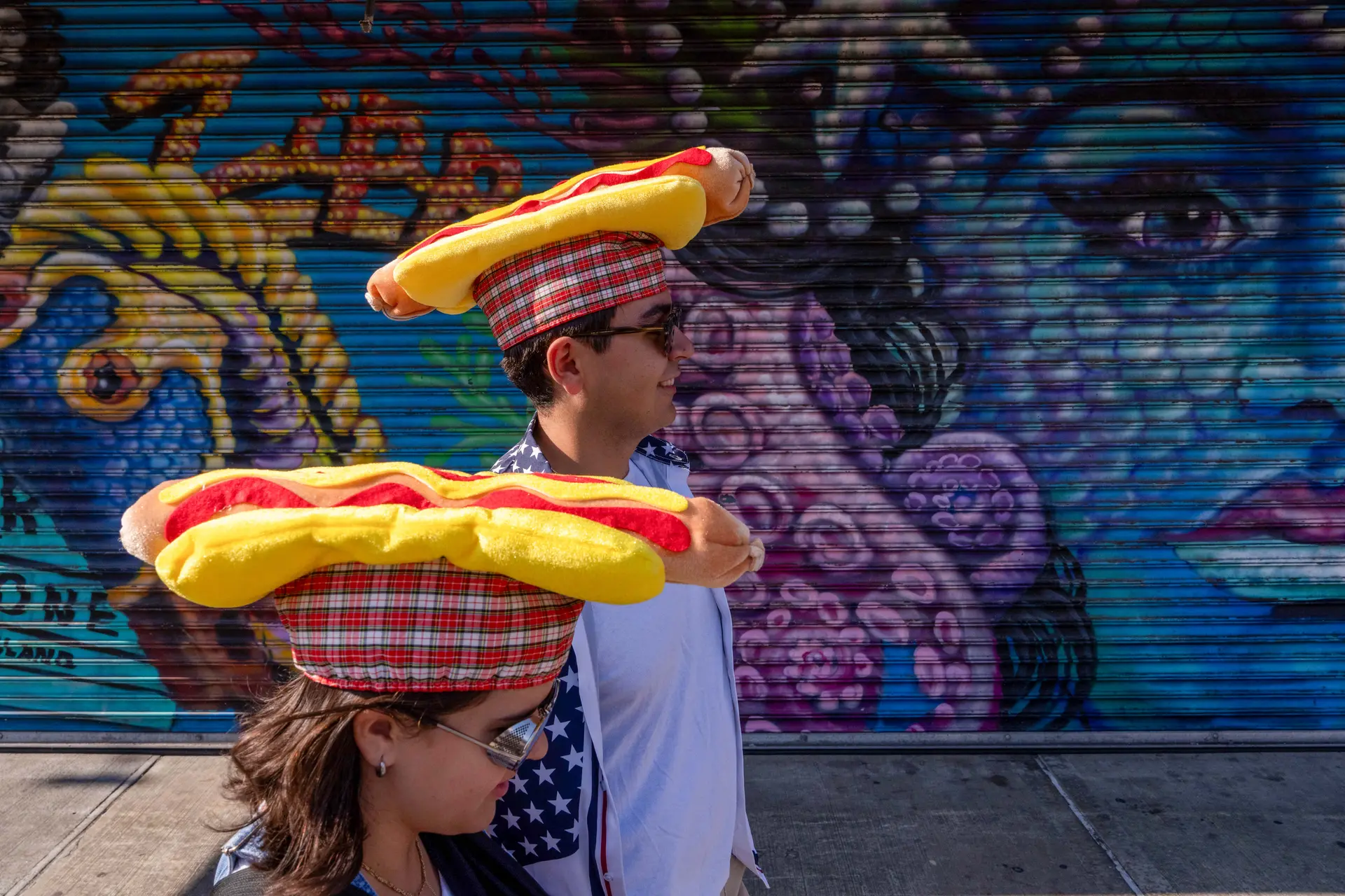 Dos personas con gorros que simulan un hot dog hacen fila para ver el Concurso Anual de Nathan para comer Hot Dog en la ciudad de Nueva York, el 4 de julio de 2025. Joey Chestnut regresa al famoso Concurso de Comer Hot Dog del 4 de Julio de Nathan para competir por su 17.ª victoria tras perderse el evento de 2024 debido a una disputa de patrocinio con Major League Eating. (Adam Gray/Getty Images)
