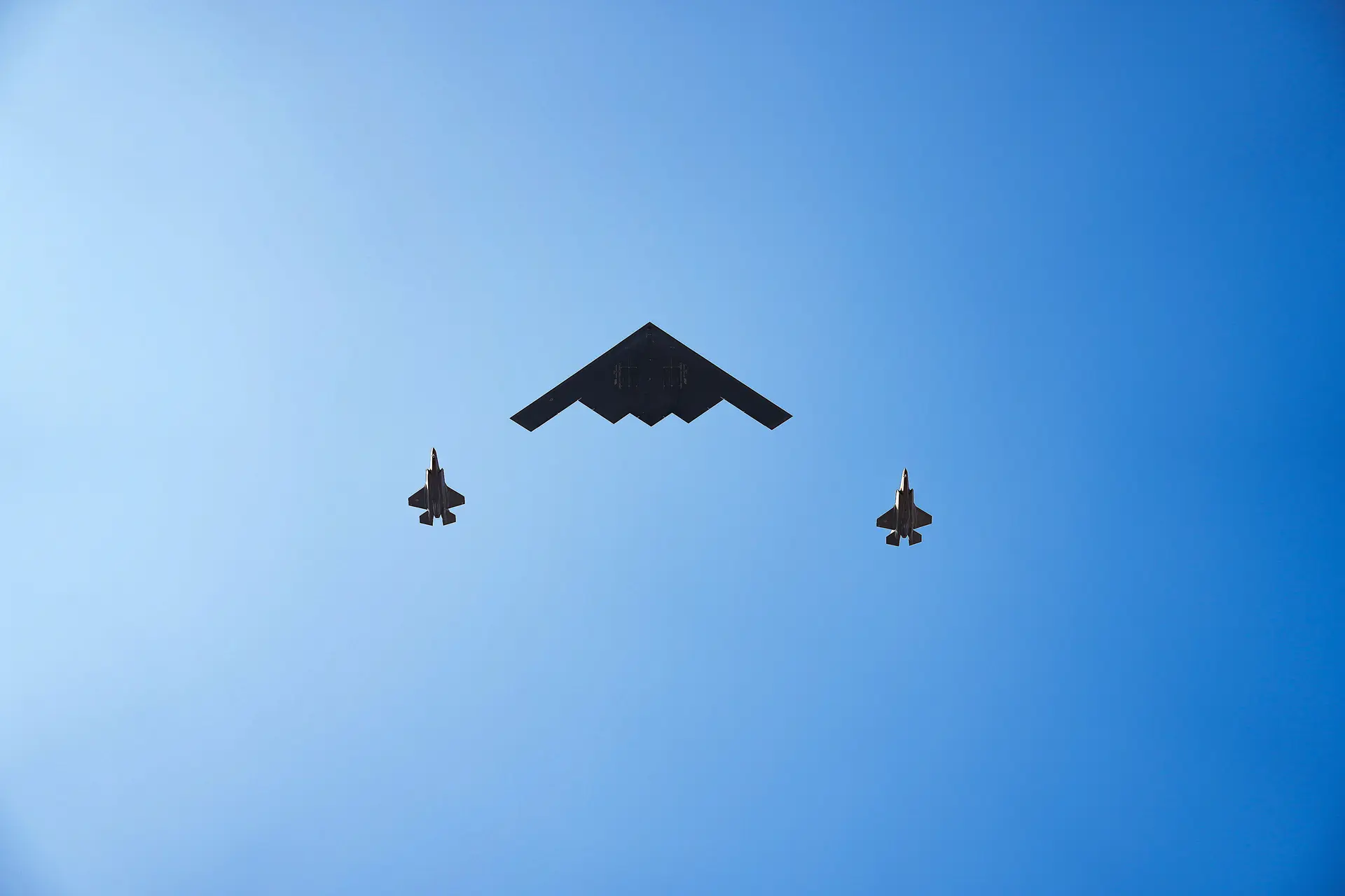 Bombarderos B-2 Spirit sobrevuelan la Casa Blanca mientras el presidente Donald Trump se pone de pie para escuchar el Himno Nacional durante un picnic familiar militar por el Día de la Independencia en el jardín sur de la Casa Blanca en Washington el 4 de julio de 2025. (Eric Lee/Getty Images)