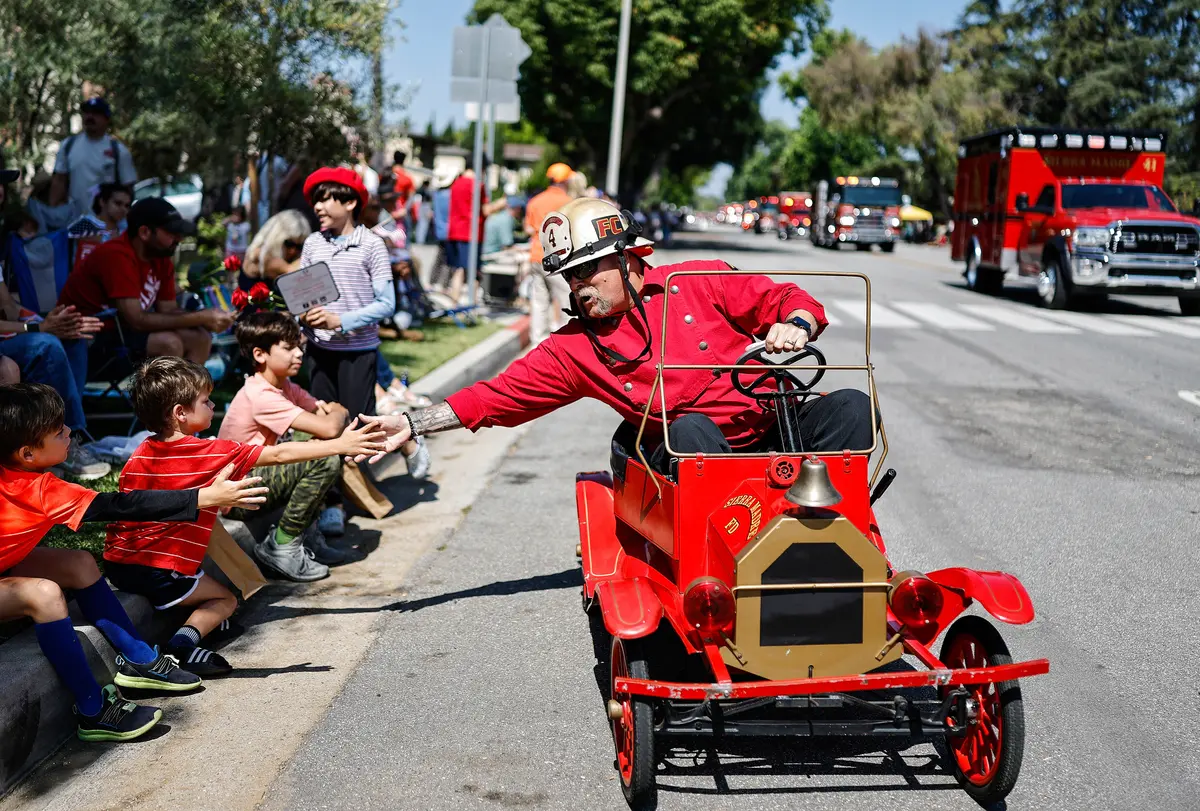 El jefe de bomberos de Sierra Madre, Brent Bartlett, saluda a niños que presencian el Desfile del Día de la Independencia de Sierra Madre, cerca de la zona afectada por el incendio de Eaton en Sierra Madre, California, el 4 de julio de 2025. En el desfile participaron bomberos, policías y otros socorristas que combatieron y respondieron a los incendios de Eaton y Palisades. El 7 de julio se cumplieron seis meses de los devastadores incendios. (Mario Tama/Getty Images)