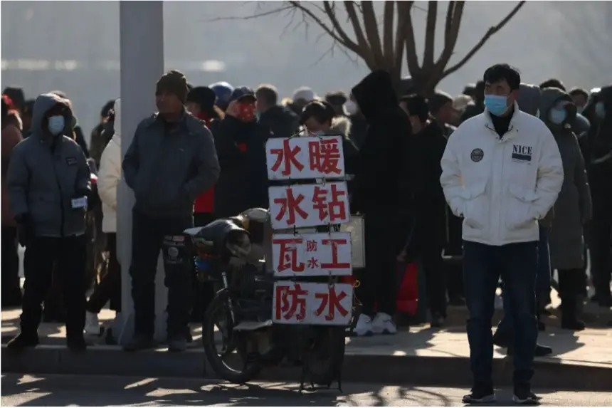 Trabajadores migrantes esperan junto a carteles que anuncian sus habilidades en una calle para ser contratados en Shenyang, provincia de Liaoning, al noreste de China, el 6 de febrero de 2023. (AFP vía Getty Images)