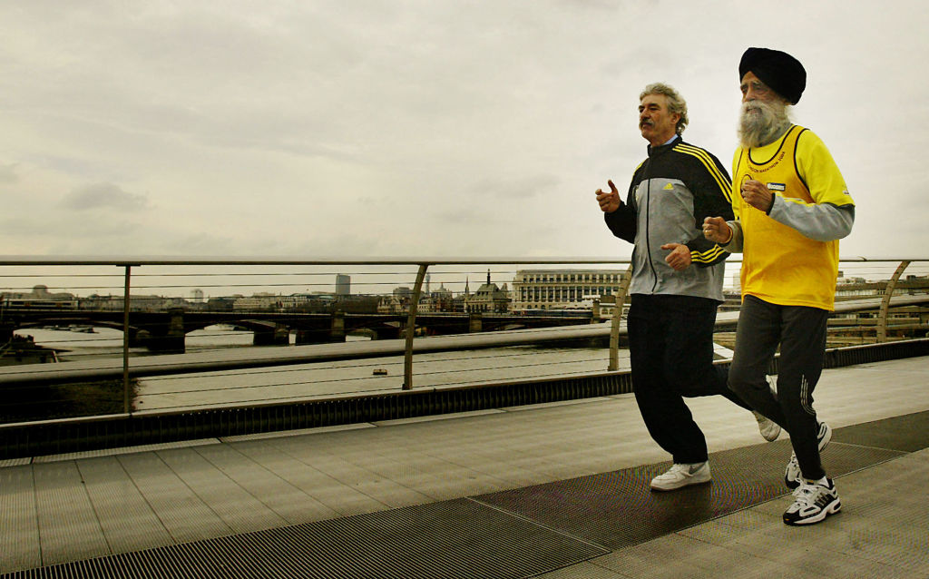 Fauja Singh (Dcha.), de 93 años, el corredor de mayor edad de la maratón Flora de Londres del 2004, corre por el Puente del Milenio en Londres junto a David Bedford, director de la maratón Flora de Londres, el 1 de abril de 2004, tras recibir un premio en reconocimiento a sus extraordinarios logros en el mundo del atletismo y celebrar su 93.º cumpleaños. (JIM WATSON/AFP a través de Getty Images)