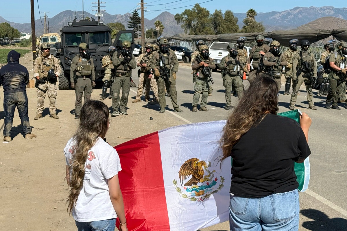 Manifestantes sostienen una bandera mexicana frente a agentes federales que bloquean una carretera durante una operación de inmigración en Camarillo, California. (Michael Owen Baker/AP Photo).