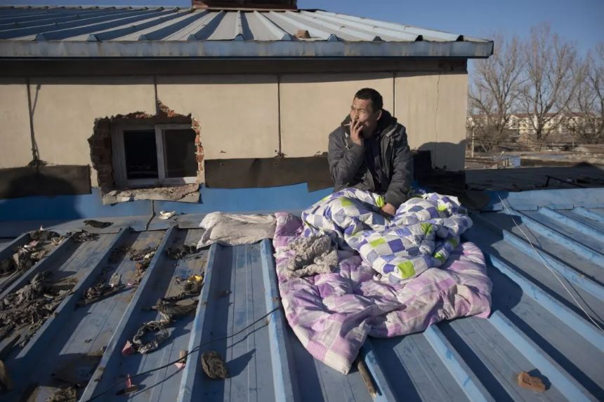 Un trabajador migrante que fue desalojado de su habitación en una zona de viviendas de bajos ingresos se sienta en el tejado de una casa donde se aloja, mientras espera recibir su salario antes de regresar a su hogar en el sur del país, en una aldea de migrantes en las afueras de Beijing, el 11 de diciembre de 2017. (Nicolas Asfouri /AFP vía Getty Images)
