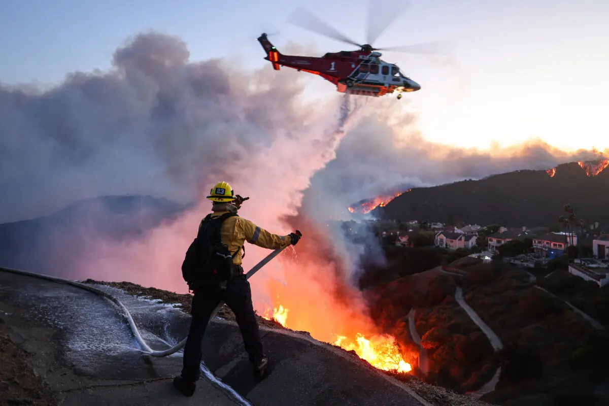 El personal de bomberos responde a las casas destruidas mientras un helicóptero arroja agua a medida que crece el incendio de Palisades en Pacific Palisades, California, el 7 de enero de 2025. (David Swanson/AFP vía Getty Images)
