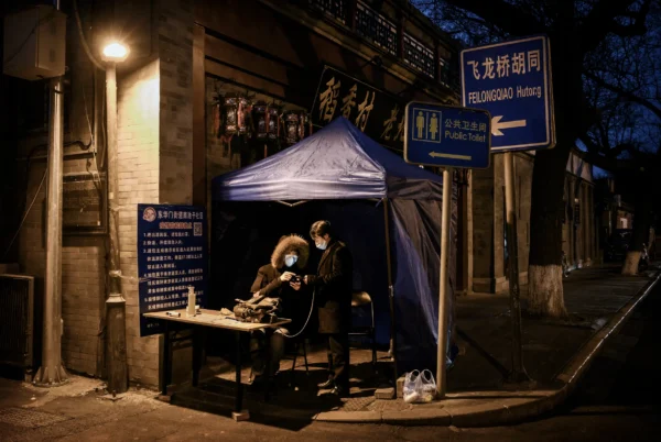 Un miembro chino del comité vecinal local lleva una máscara protectora mientras comprueba la identificación de un hombre que llega a una zona de Beijing el 28 de febrero de 2020. Durante la pandemia de COVID-19, Shi no pudo salir del edificio en el que vivía porque no podía pasar los controles sin presentar un documento de identidad, con el que la policía habría conocido su ubicación. (Kevin Frayer/Getty Images)