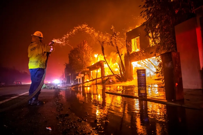 Un bombero lucha contra el incendio de Palisades, que quema casas en la autopista Pacific Coast Highway durante una fuerte tormenta de viento en Los Ángeles, el 8 de enero de 2025. El incendio forestal duró 24 días, causó la muerte de 12 residentes, obligó a miles de personas a evacuar sus hogares y dejó barrios enteros inhabitables. (Apu Gomes/Getty Images)