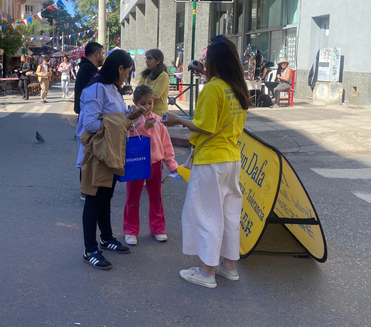 <em>Visitantes conocen sobre la persecución a Falun Dafa y los principios de Verdad, Benevolencia y Tolerancia prohibidos por el PCCH en las flores que los manifestantes entregaron al público durante la feria Palmear, en Asunción, Paraguay, el 20 de julio de 2025. (The Epoch Times)</em>