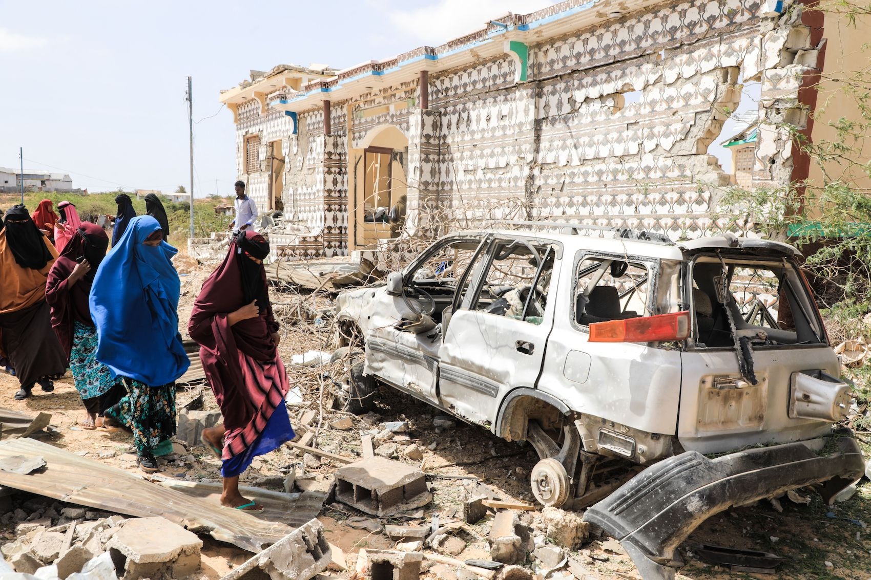 Mujeres caminan junto a una casa destruida y los restos de un automóvil tras una explosión provocada por terroristas de Al-Shabaab durante un ataque a una comisaría en las afueras de Mogadiscio, Somalia, el 16 de febrero de 2022. (Hassan Ali Elmi/AFP a través de Getty Images).