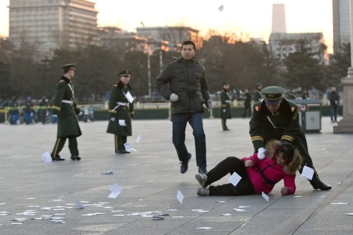 Una demandante es empujada al suelo por un policía paramilitar después de correr hacia una zona acordonada cerca de un mástil con la bandera nacional en la plaza de Tiananmen y lanzar panfletos para protestar por su caso de injusticia, en Beijing, el 5 de marzo de 2014. (Alexander F. Yuan /AP Photo)