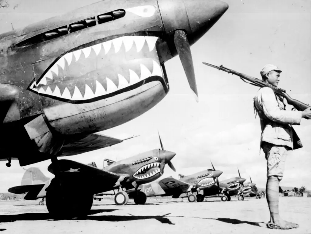 Un soldado chino vigila una fila de aviones de combate estadounidenses P-40, pintados con el emblema de la cara de tiburón de los "Tigres Voladores", en un aeródromo en algún lugar de China, alrededor de 1942. (Dominio público)