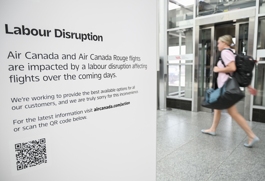 MONTREAL (Canadá), 14/08/2025.- Una mujer pasa junto a un cartel de Air Canada que advierte sobre una posible interrupción laboral en el Aeropuerto Internacional Montreal-Trudeau, en Montreal, Quebec, Canadá, el 14 de agosto de 2025. Air Canada se enfrenta a un cierre casi total, ya que el sindicato planea declararse en huelga tras el fracaso de las negociaciones con los auxiliares de vuelo por el tema de los salarios y el trabajo no remunerado. (EFE/EPA/GRAHAM HUGHES)