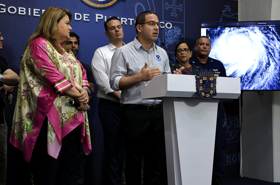 SAN JUAN (PUERTO RICO), 17/08/2025.- La gobernadora de Puerto Rico Jenniffer Gonzalez (i) escucha al meteorólogo del Centro Nacional de Meteorología Ernesto Rodríguez (c) durante una rueda de prensa este domingo, en La Fortaleza (sede de Gobierno) en San Juan (Puerto Rico). Erin rebajó su intensidad durante la madrugada hasta convertirse en un huracán de categoría 3 en la escala Saffir-Simpson, con vientos máximos sostenidos de 205 kilómetros por hora mientras sus bandas exteriores llevan intensas lluvias a Puerto Rico y las Islas Vírgenes, informó el Centro Nacional de Huracanes (NHC, en inglés) de EE.UU. (EFE/ Thais Llorca)