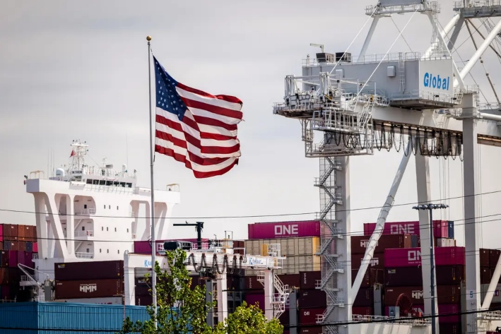 La bandera estadounidense ondea sobre contenedores de carga en Port Liberty, en Bayonne (Nueva Jersey), el 7 de agosto de 2025. Los legisladores han propuesto un proyecto de ley para aumentar las sanciones por infracciones comerciales y permitir al Gobierno estadounidense emprender acciones legales contra importadores extranjeros en nombre de empresas estadounidenses. (Spencer Platt/Getty Images)