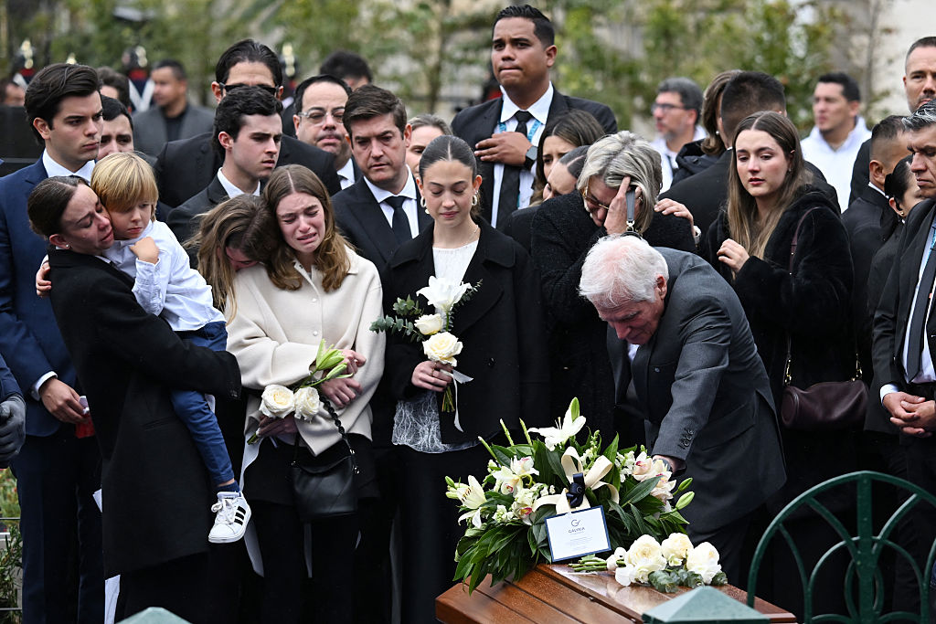 Miguel Uribe Londoño (Der.), padre del candidato presidencial colombiano asesinado Miguel Uribe, toca el féretro de su hijo mientras su nuera, la viuda María Claudia Tarazona (Izq.) con su hijo en brazos, entre otros familiares, lloran durante el entierro en el Cementerio Central de Bogotá, el 13 de agosto de 2025. (RAUL ARBOLEDA/AFP vía Getty Images)