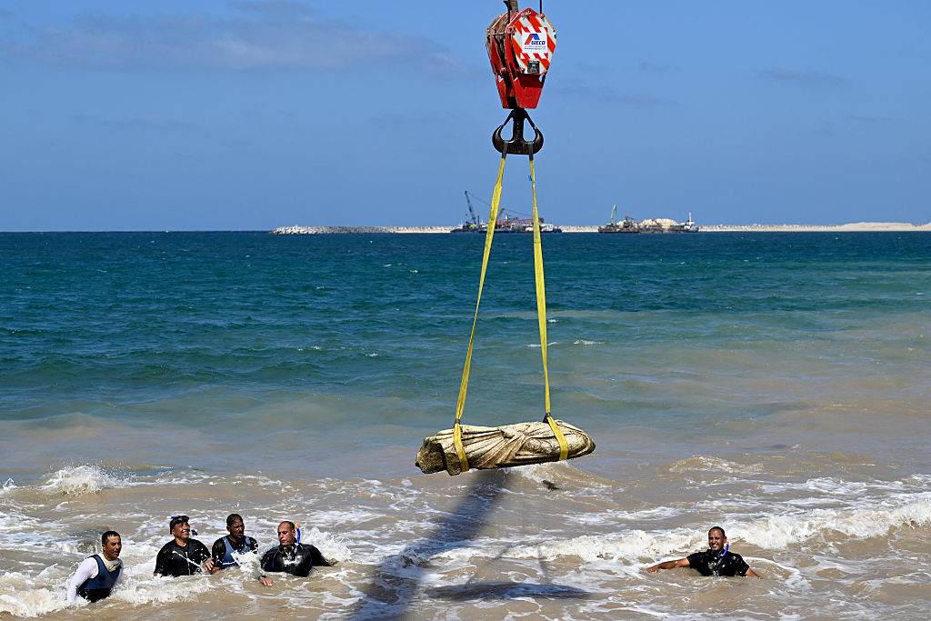Los buzos observan cómo una grúa saca una estatua de las aguas de la bahía de Abu Qir, en Alejandría, el 21 de agosto de 2025, como parte de un evento organizado por el Ministerio de Turismo y Antigüedades para recuperar antigüedades hundidas. (KHALED DESOUKI/AFP a través de Getty Images)