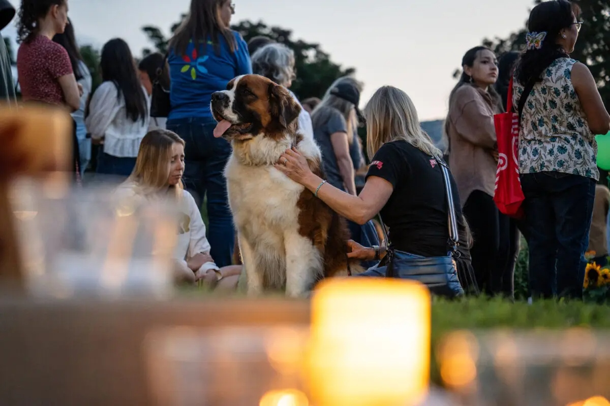 Kate Campo (derecha), propietaria de un negocio en el barrio, sentada con su perro, se une a otras personas para llorar la muerte de los dos escolares que fueron asesinados el día anterior durante el tiroteo en la escuela católica Annunciation Catholic School en Minneapolis el 28 de agosto de 2025. (Madalina Kilroy/The Epoch Times)