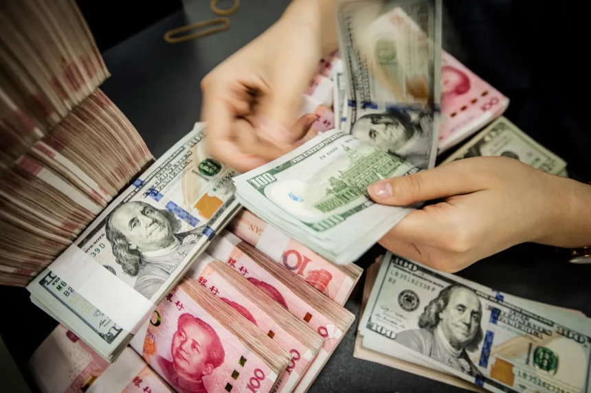 Un empleado de un banco chino cuenta billetes de 100 yuanes y de 100 dólares estadounidenses en un mostrador bancario en Nantong, provincia de Jiangsu, China, el 6 de agosto de 2019. (STR/AFP vía Getty Images)