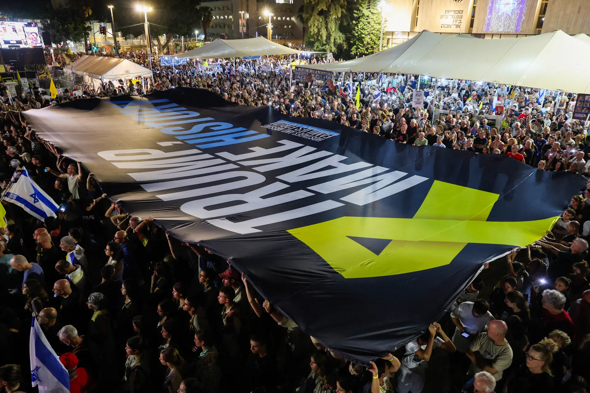Manifestantes levantan una gran pancarta durante una manifestación organizada por las familias de israelíes secuestrados por terroristas de Hamás en la Franja de Gaza, para exigir su liberación y un alto el fuego en la guerra en Gaza, en la Plaza de los Rehenes de Tel Aviv, el 30 de agosto de 2025. (Jack Guez/AFP vía Getty Images)