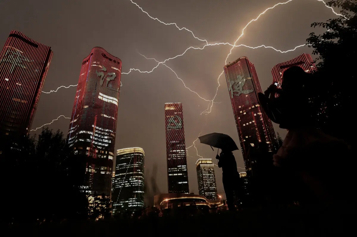 Un rayo atraviesa el cielo mientras la gente contempla los edificios que proyectan un espectáculo de luces en la víspera del centenario del Partido Comunista Chino en Beijing, el 30 de junio de 2021. (Noel Celis/AFP a través de Getty Images)