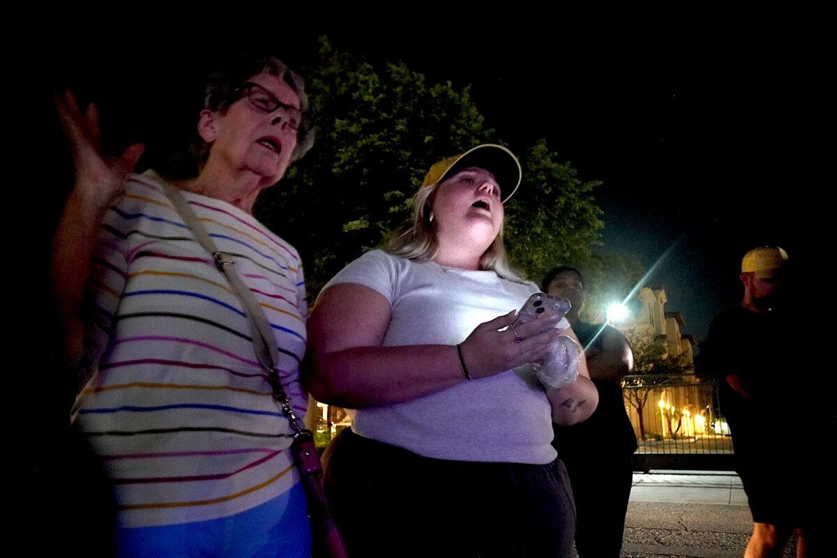 Betty (izquierda) y su nieta Riley (derecha) cantan Amazing Grace frente a la sede de Turning Point USA en Phoenix el 10 de septiembre de 2025. (Allan Stein/The Epoch Times)