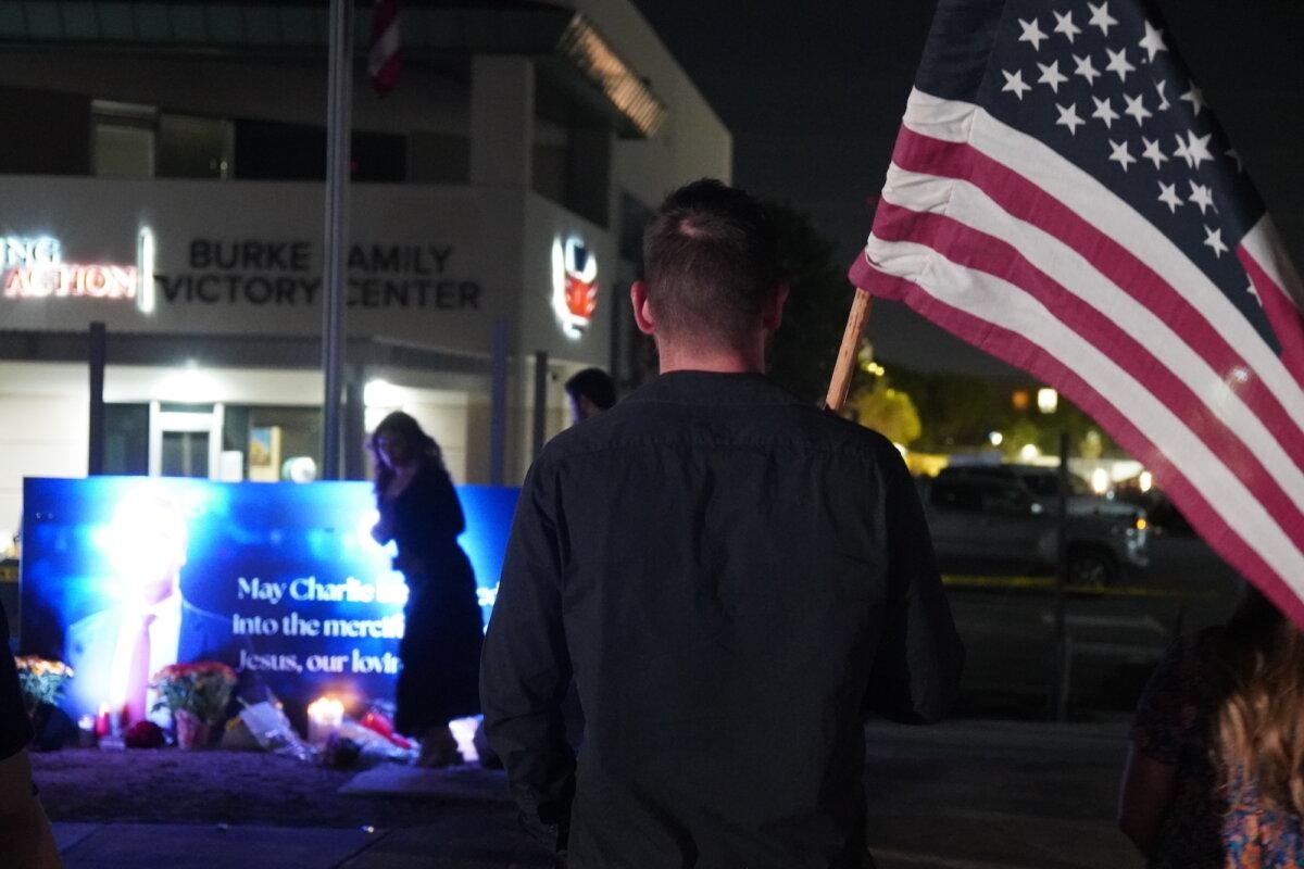 Un hombre con una bandera estadounidense delante de una pancarta iluminada en honor al fundador de Turning Point USA, Charlie Kirk, asesinado en Phoenix, Arizona, el 10 de septiembre de 2025. (Allan Stein/The Epoch Times)