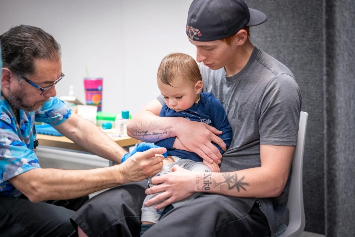 Un hombre sostiene a su hijo de 14 meses mientras le administran la vacuna triple vírica en una clínica de Lubbock, Texas, el 1 de marzo de 2025. Algunos padres han informado que creen que las vacunas pueden causar autismo. (Jan Sonnenmair/Getty Images)