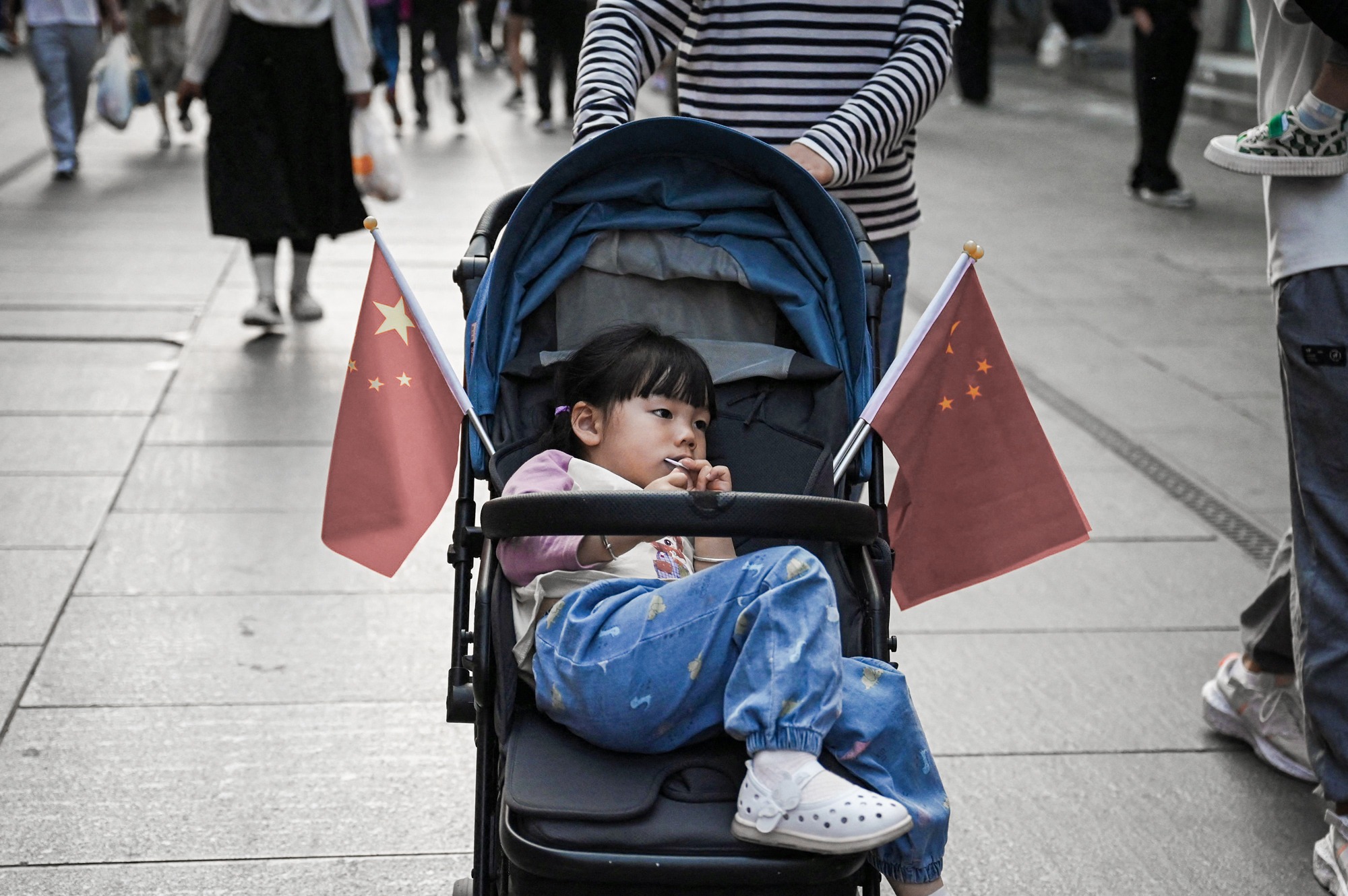 Una niña descansa en un cochecito adornado con banderas chinas mientras su madre la pasea por la zona de Qianmen, en Pekín, el 3 de mayo de 2023. Según la División de Población de las Naciones Unidas, en 2023 la tasa de natalidad de China había caído por debajo de un hijo por mujer. (Greg Baker/AFP a través de Getty Images).